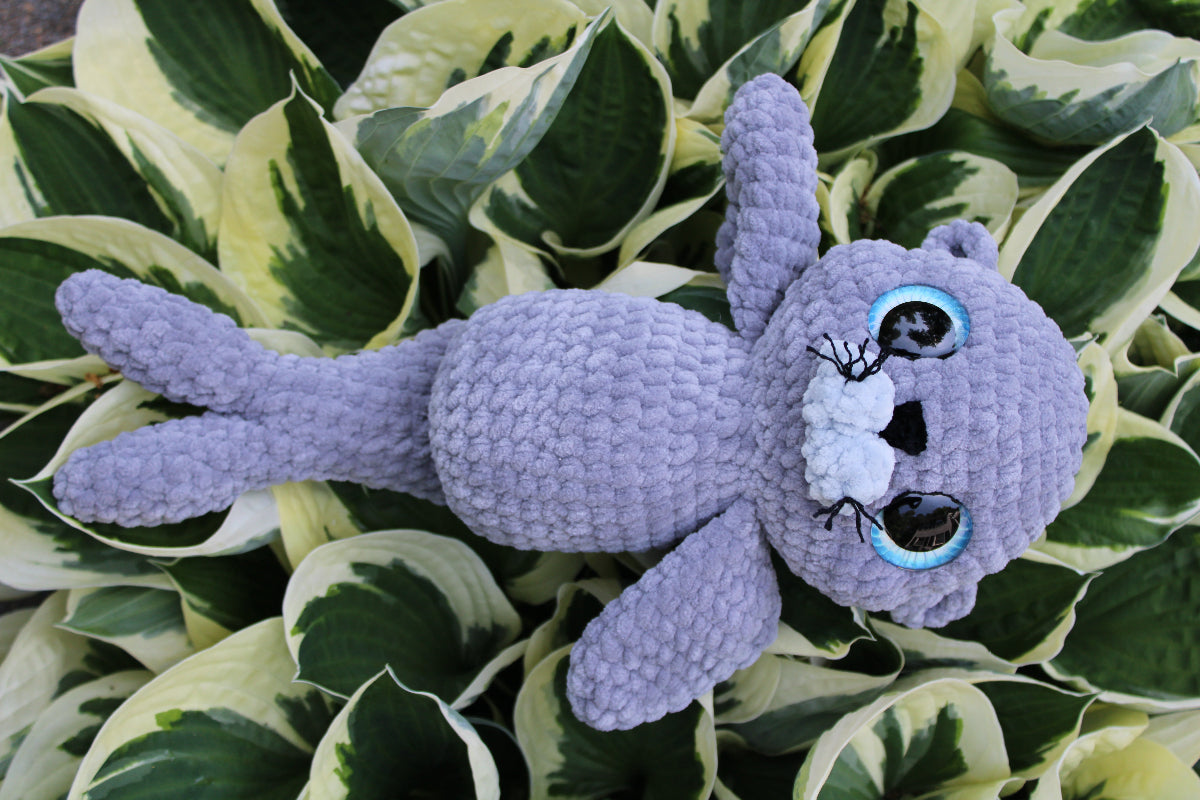 Gray plush toy with a white face on a leafy green background