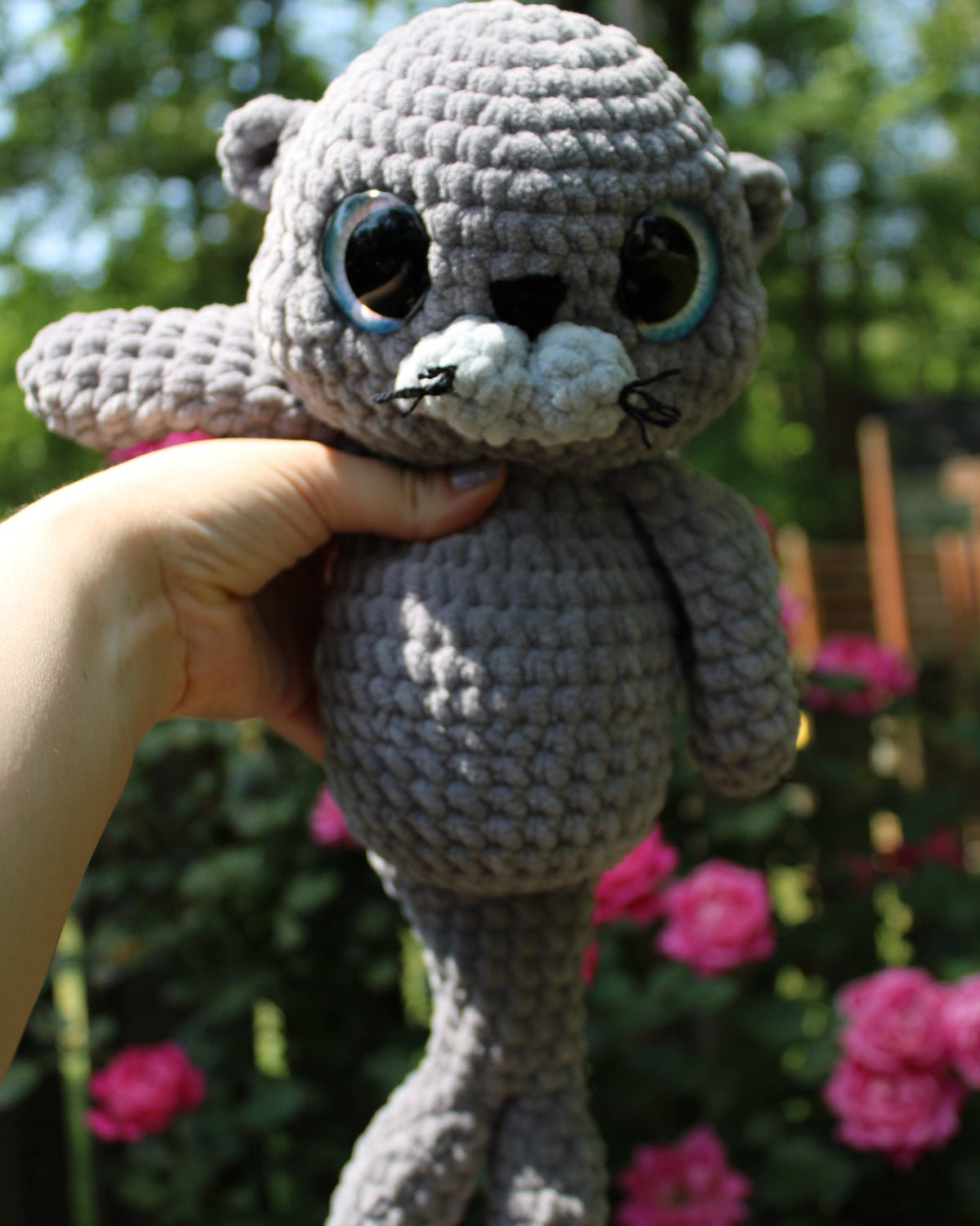 Crocheted sea lion otter plush toy held by a hand with a garden background
