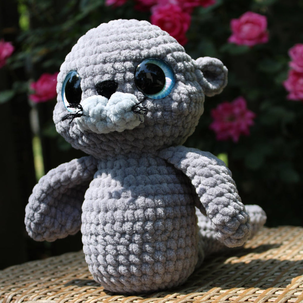 Crocheted seal toy on a wicker surface with pink flowers in the background