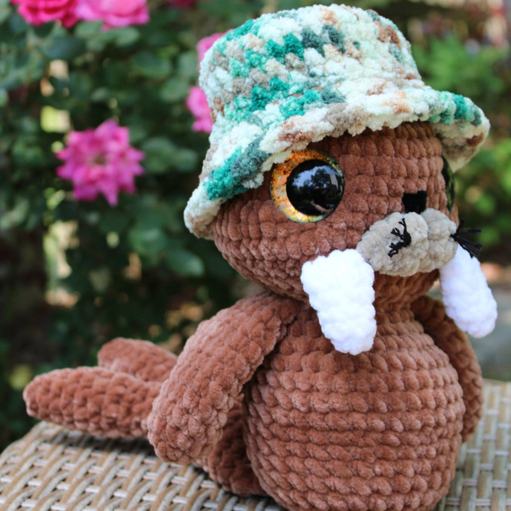 Crocheted animal toy with a hat in front of pink flowers