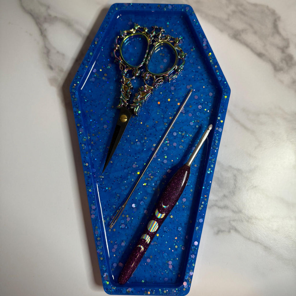 Decorative coffin-shaped tray with scissors and crochet hooks on a marble surface